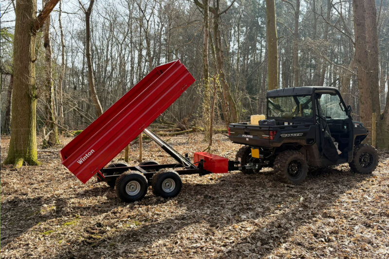 Polaris Ranger utility vehicle with a red dump trailer raised in a forest clearing.