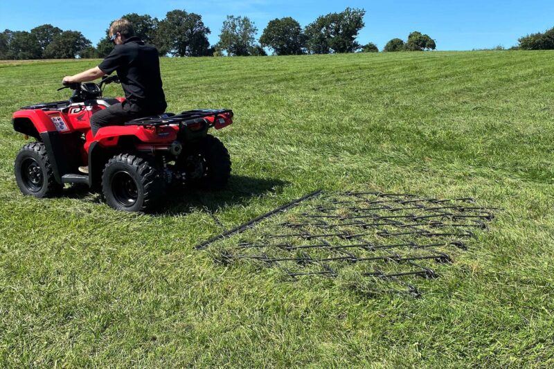 Man in a black shirt rides a red Honda ATV across a sunny grassy field.