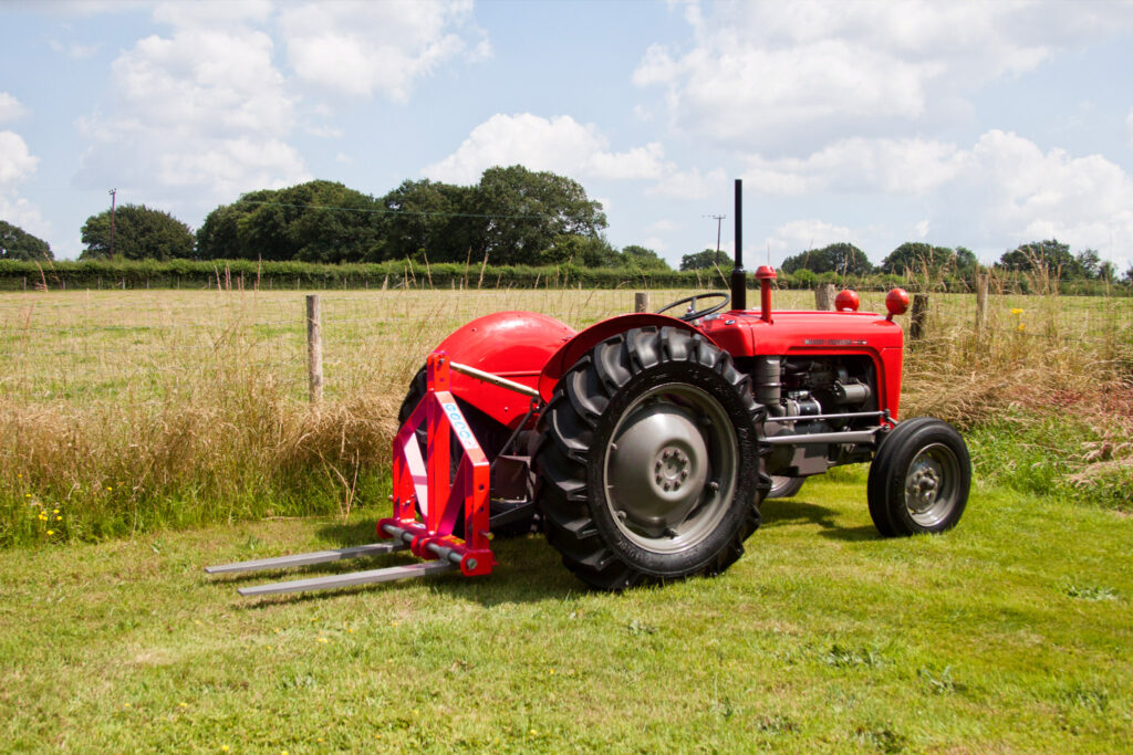 Red Massey Ferguson tractor with a front-mounted mower in a grassy field under a cloudy blue sky.
