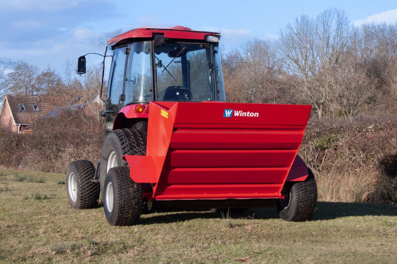 Front view of a large red tractor on a grassy field, with oversized treaded tires and a Winton logo on the side panel.