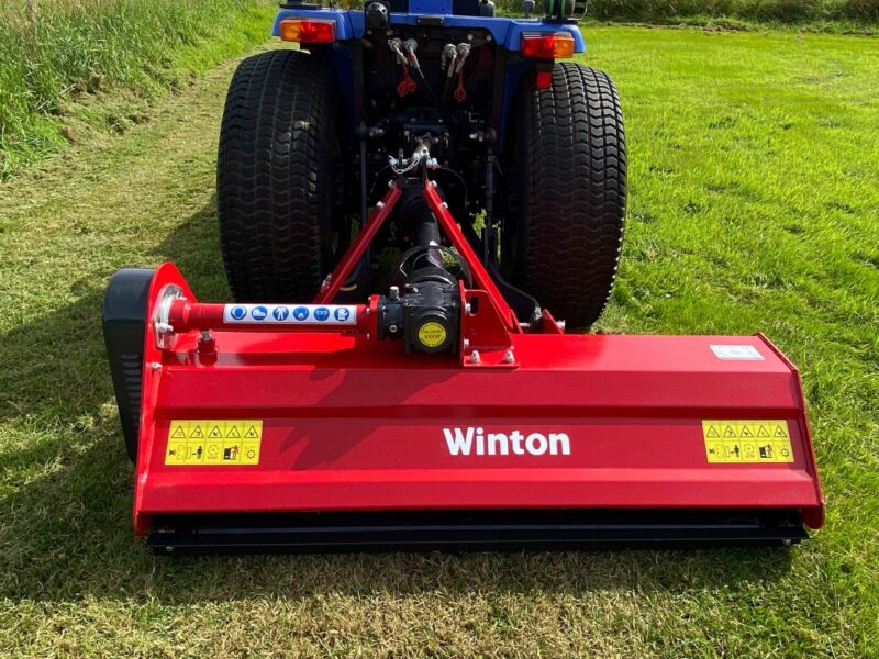 Rear view of a red Winton agricultural attachment with large dual tires, hydraulic hoses, and warning stickers on grass field