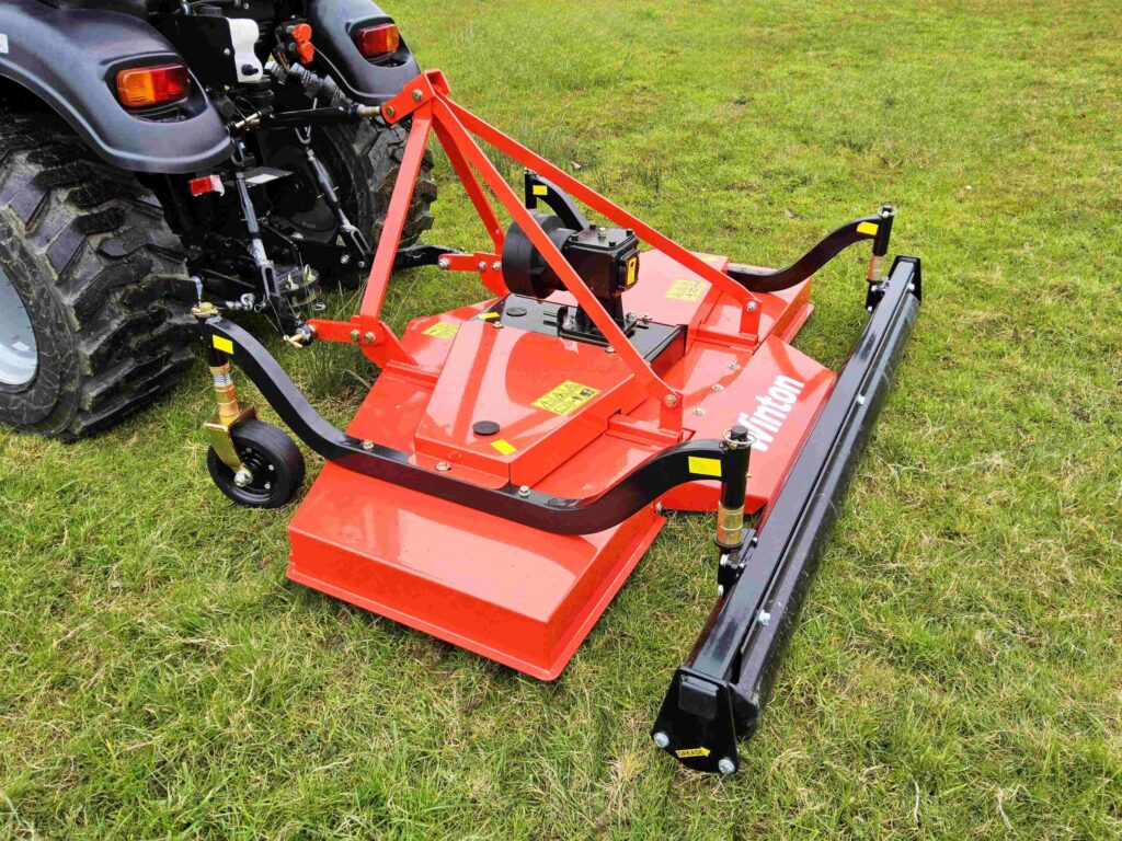 Rear-mounted red mower attachment connected to a tractor, ready to cut grass on a field.