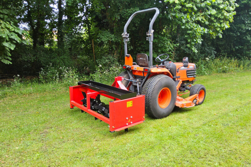 Orange tractor with a large red front-mounted implement, parked on a grassy area with trees in the background.