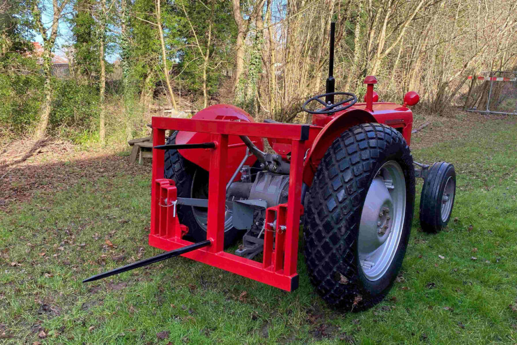 Red tractor with front fork attachment parked on a grassy yard beside trees, outdoors.