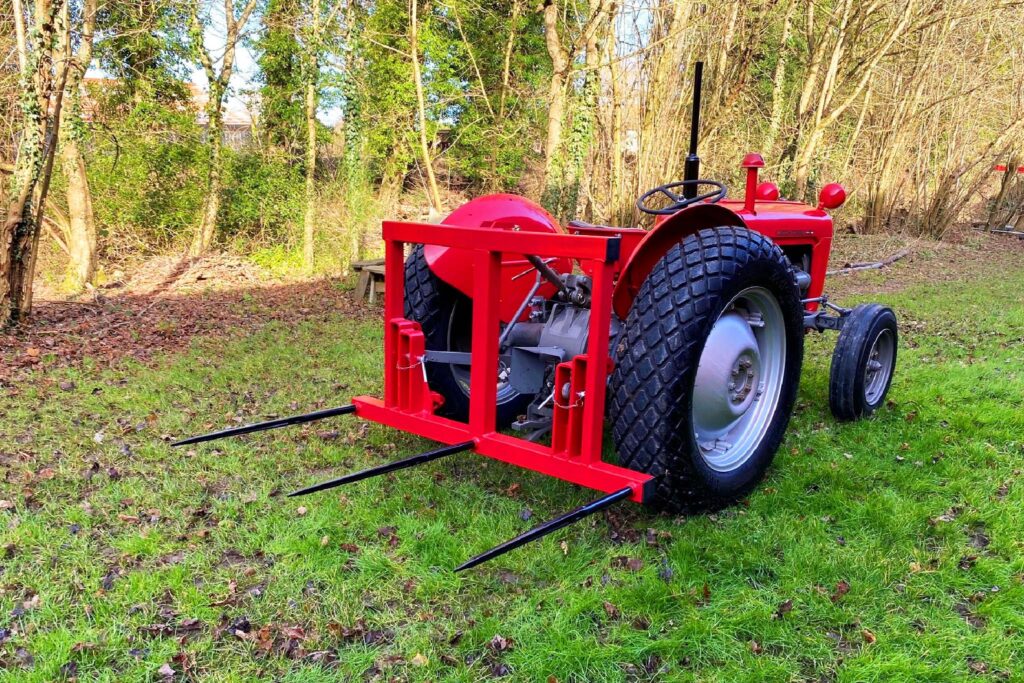 Red tractor with black-tired wheels and vineyard-style hitch in a grassy, tree-filled yard.