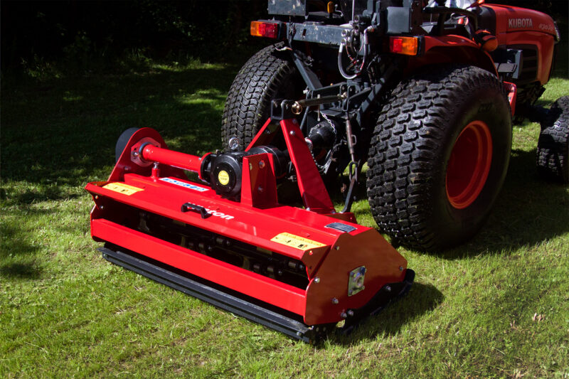 Close-up of a red mower attachment connected to a Kubota tractor on a grassy field, showing large tires nearby.