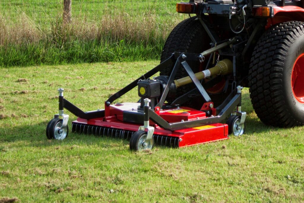 Red lawn mower/attachment with large rear tires parked on a grassy field