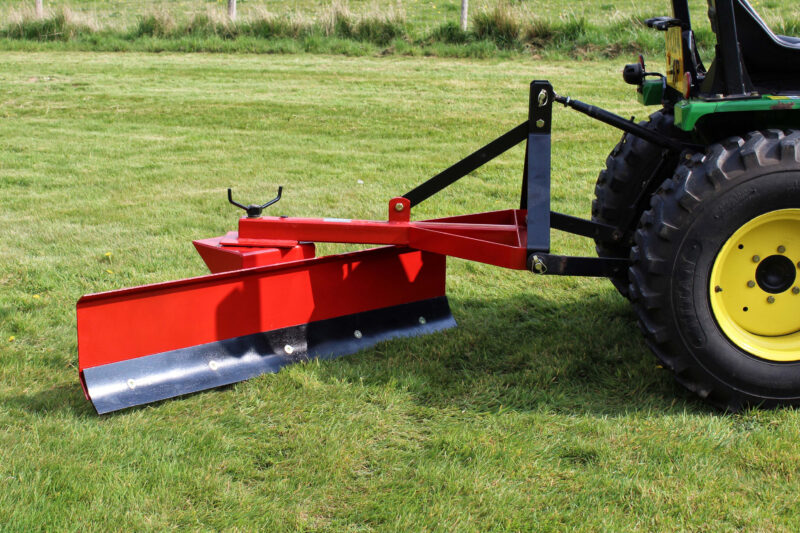 Tractor with a red mowing implement attached, parked on a grassy field.