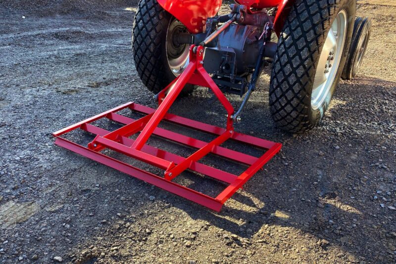 Red metal frame stabilizing a wheeled axle on a gravel surface, likely a trailer or maintenance stand with large tires