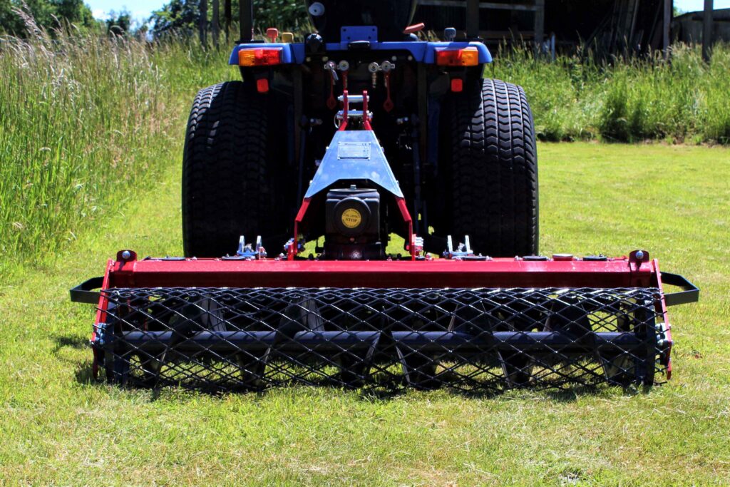 Rear view of a red farming implement with oversized tires and a blue frame in a sunlit grassy field
