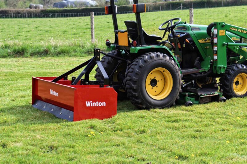 Green John Deere tractor with a large red Winton mowing attachment on a grassy field.**(informative)