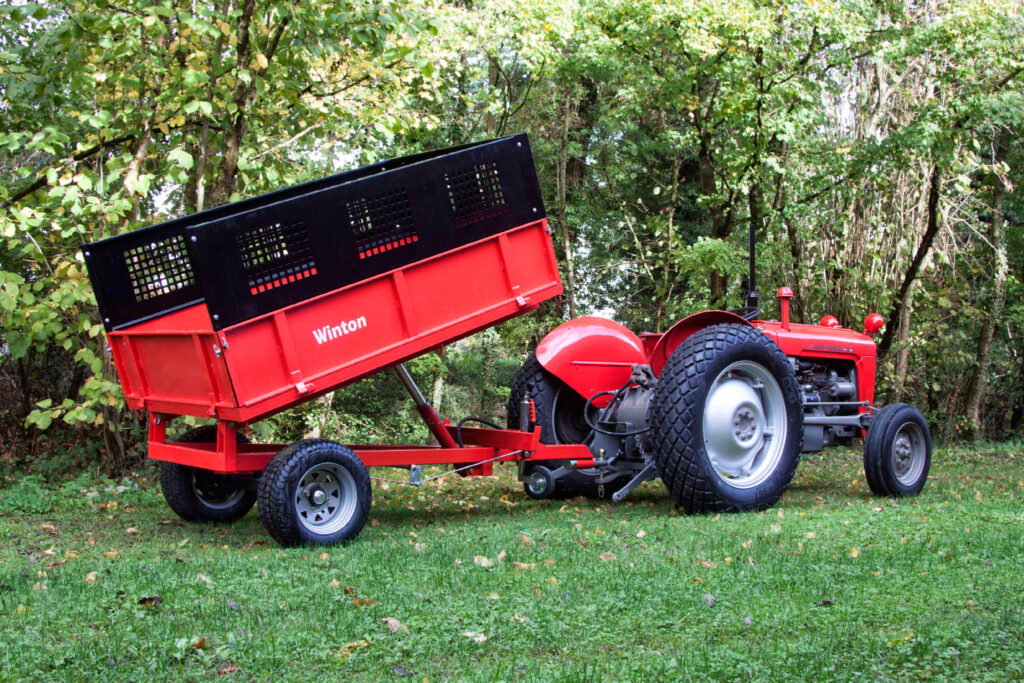 Red tractor with a tipped red trailer on a grassy area, trees in the background.
